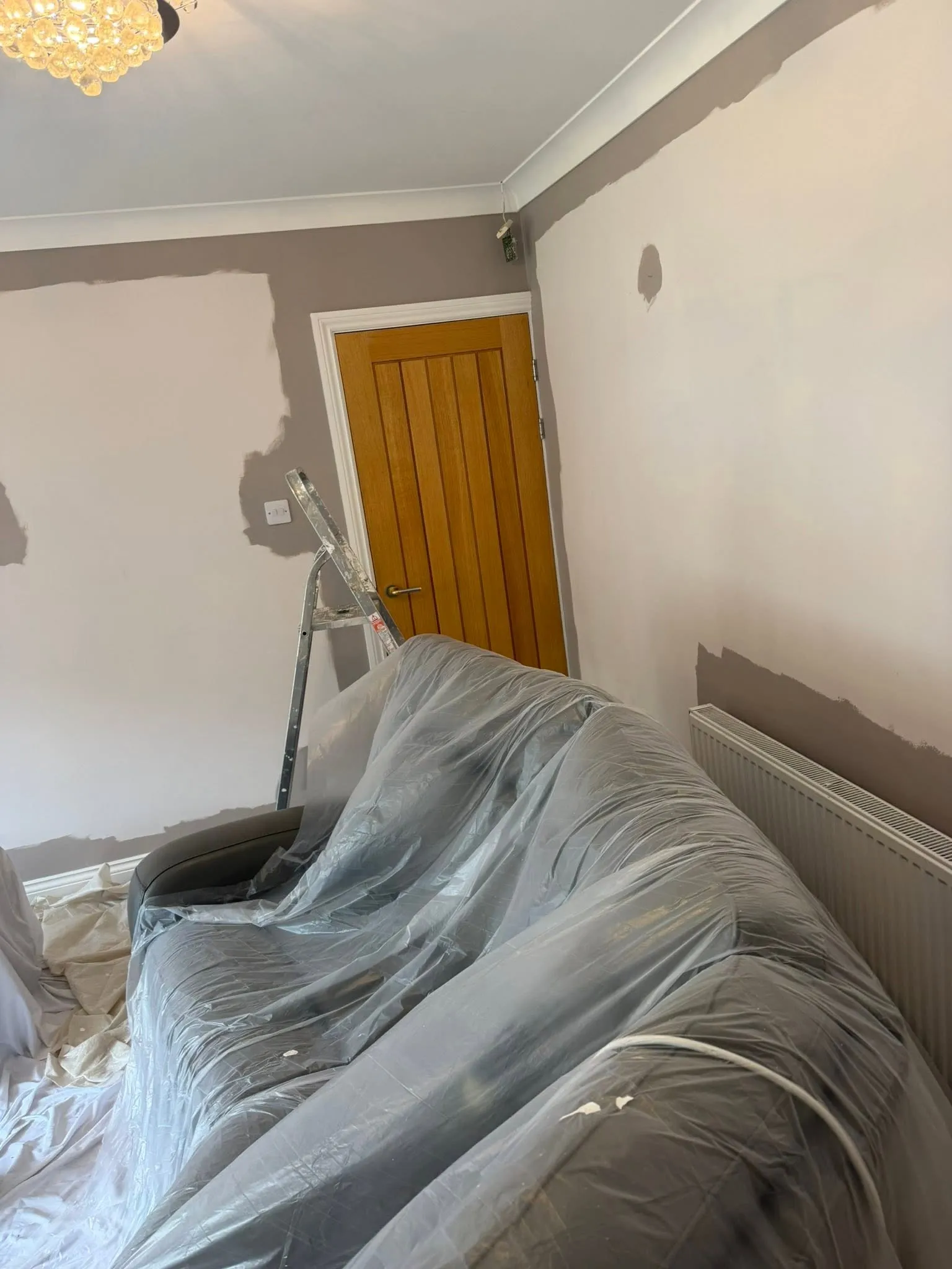 Bedroom being painted grey-brown, with furniture covered in plastic sheeting and an oak door