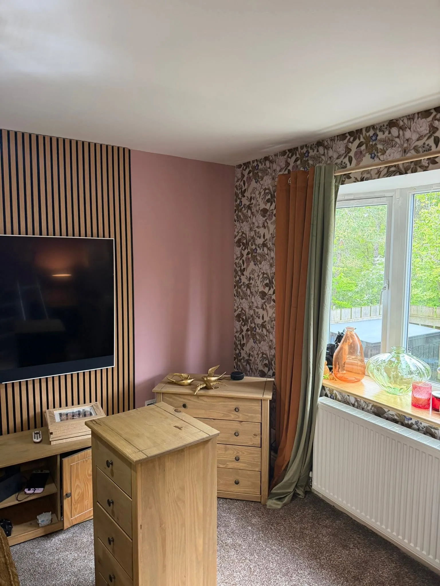 Living room decorated with a slat wall, pink paint and floral wallpaper