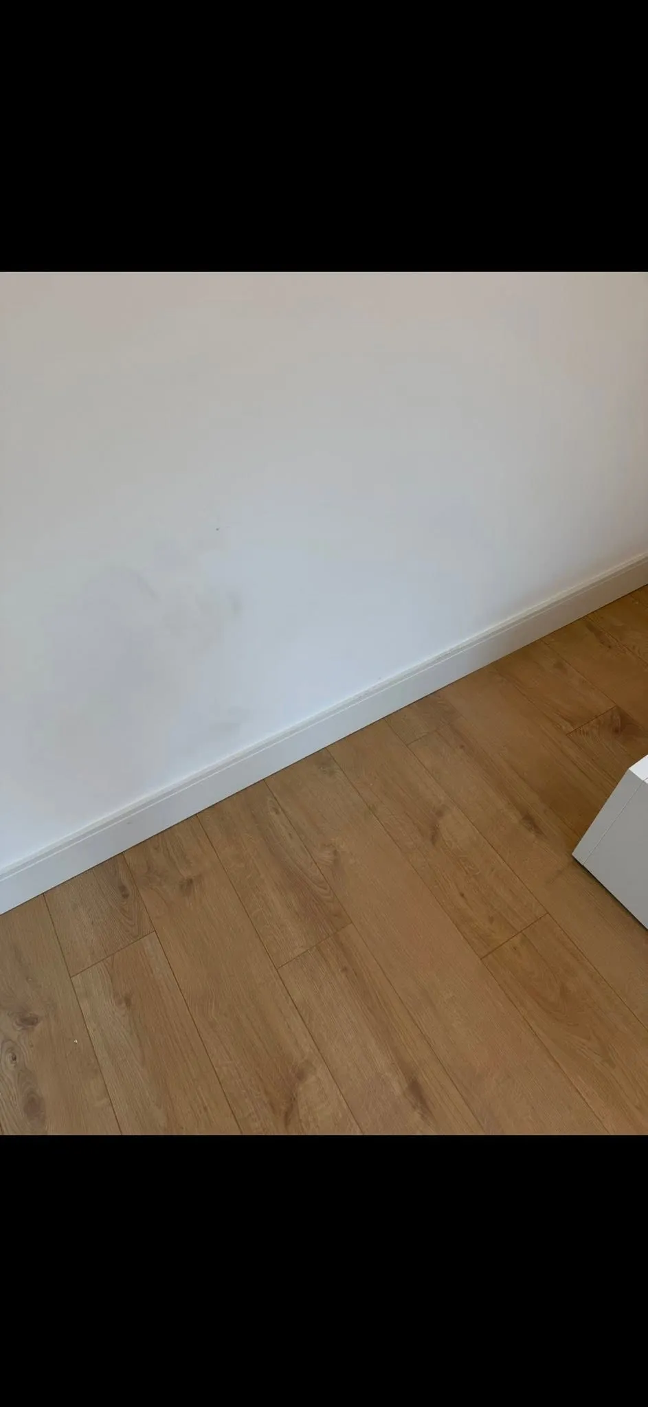 Detail of white skirting board fitted neatly against new laminate flooring