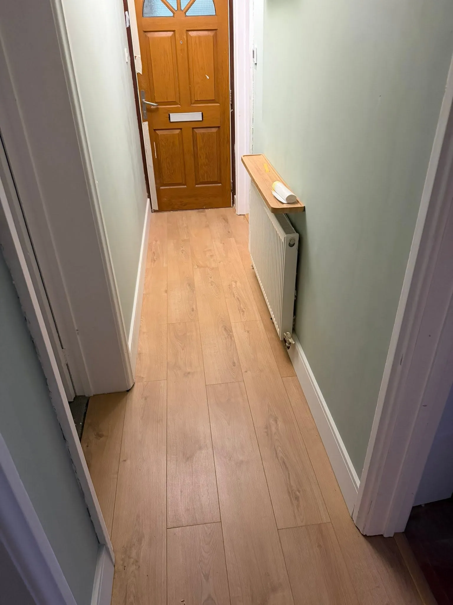 Hallway painted sage green with light wood-effect flooring leading to the front door