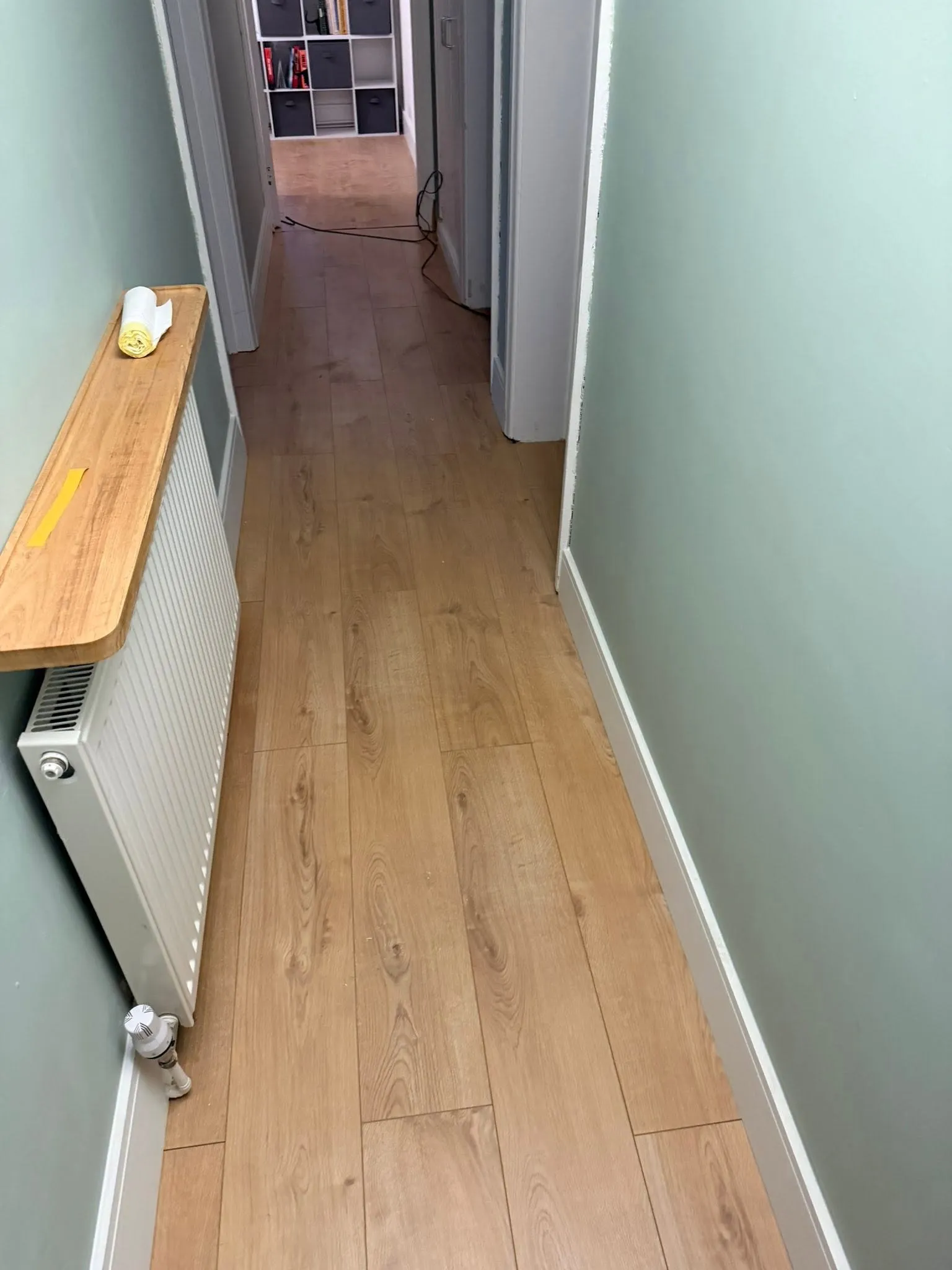 The same hallway painted sage green with new oak-effect laminate flooring and white skirting