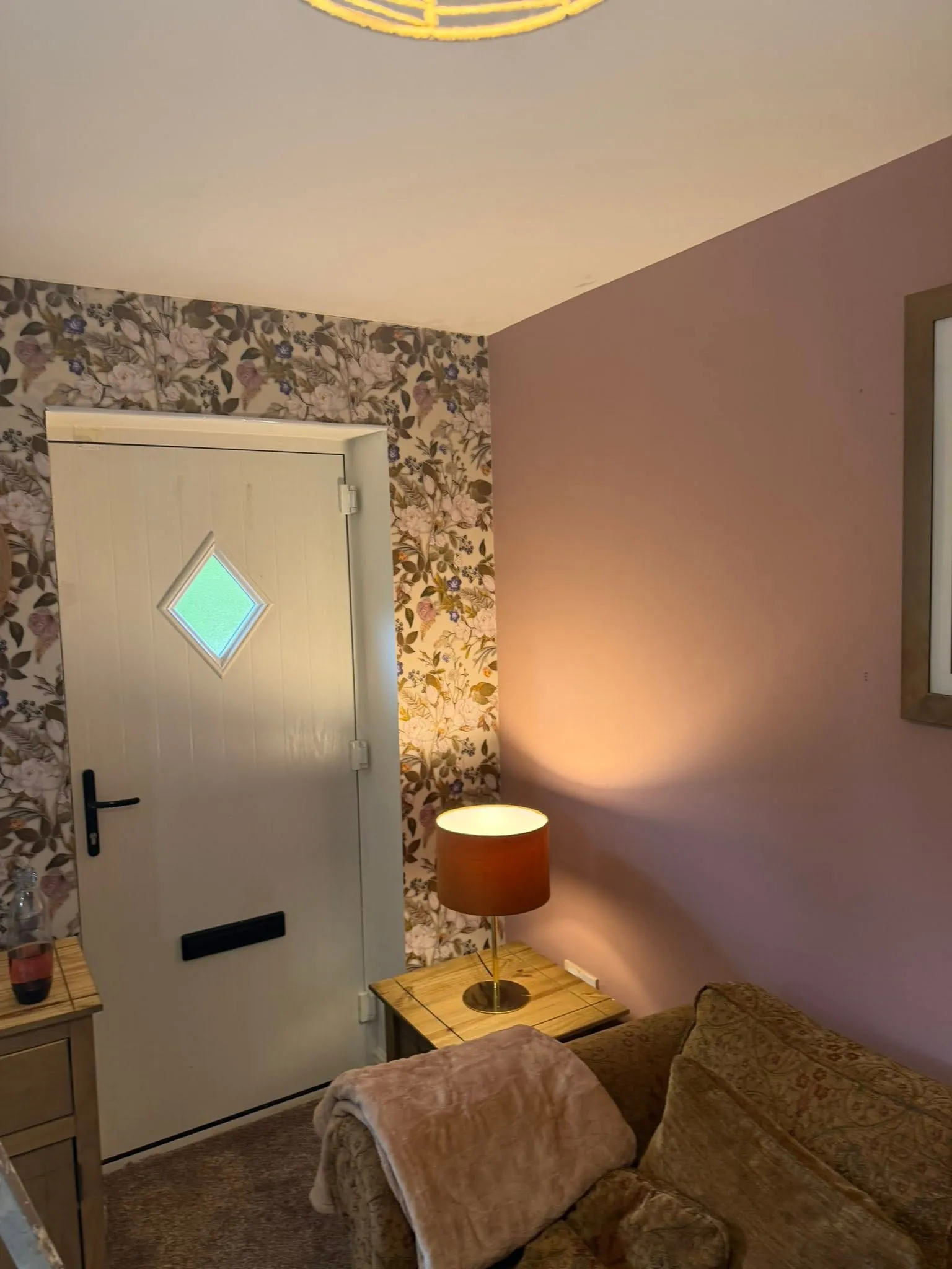 Small room decorated with a mauve wall and floral wallpaper beside a white front door
